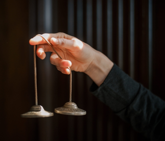 Hand holding two string-connected spinning tops against a dark background curtain.