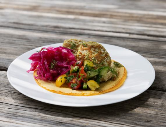 Crispy taco on a corn tortilla topped with diced vegetables and herbs, with pink pickled cabbage slaw on the side, served on a white plate.