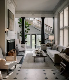 Elegant living room with black columns, a grand staircase, and ornate plaster molding; a glass lantern hangs above the entryway.