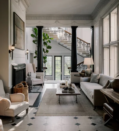 Elegant living room with black columns, a grand staircase, and ornate plaster molding; a glass lantern hangs above the entryway.