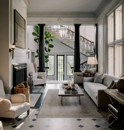 Elegant living room with black columns, a grand staircase, and ornate plaster molding; a glass lantern hangs above the entryway.