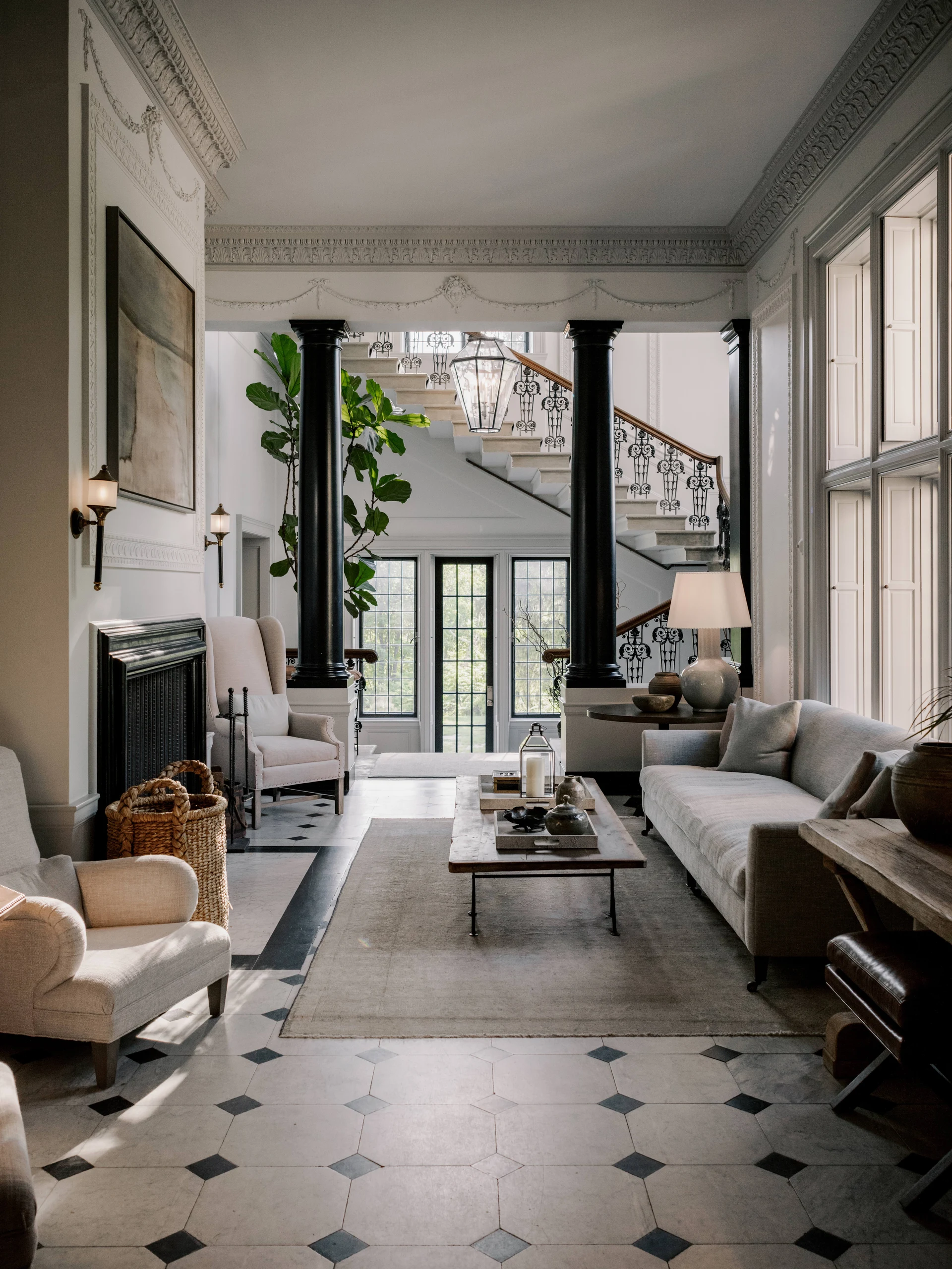 Elegant living room with black columns, a grand staircase, and ornate plaster molding; a glass lantern hangs above the entryway.