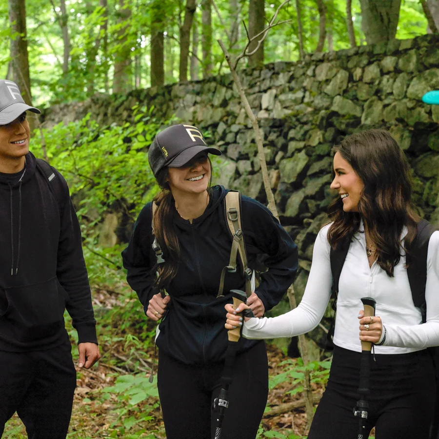 Group of hikers standing on a forest trail, wearing backpacks and trekking poles, smiling and talking.