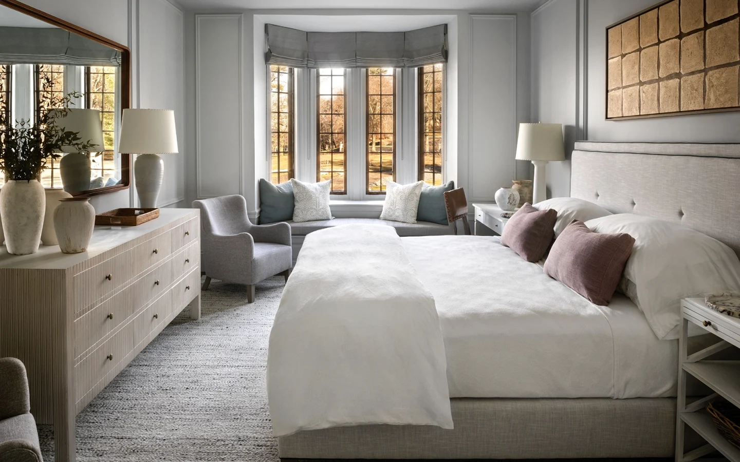 Bright, elegant bedroom with a bay-window seating area, two white beds, and neutral gray furnishings.