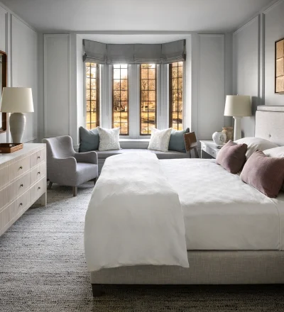 Bright, elegant bedroom with a bay-window seating area, two white beds, and neutral gray furnishings.