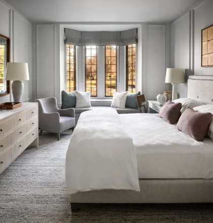 Bright, elegant bedroom with a bay-window seating area, two white beds, and neutral gray furnishings.