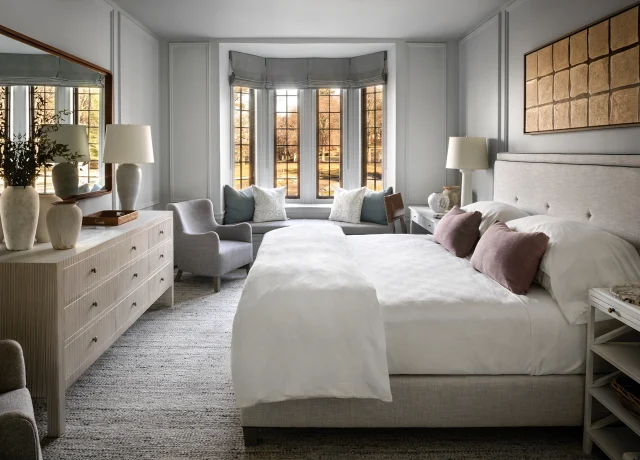 Bright, elegant bedroom with a bay-window seating area, two white beds, and neutral gray furnishings.