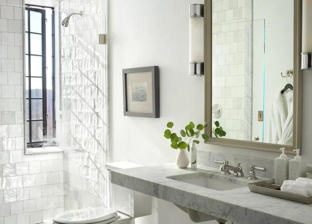 Bright white bathroom with a marble vanity, large mirror, and two wall sconces above a checkered black-and-white floor.