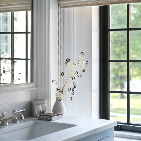 White kitchen window with striped Roman blinds and a marble counter, featuring a vase of dried flowers nearby.