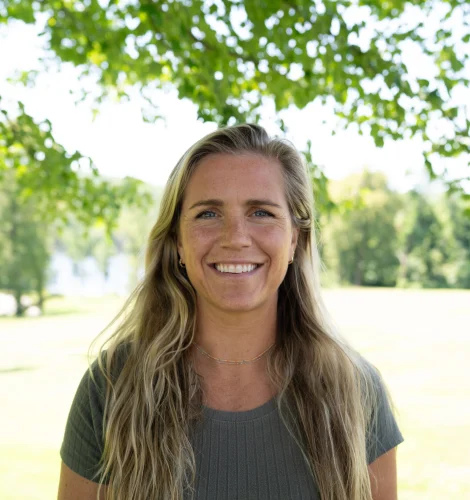 Smiling woman outdoors with green trees in the background.