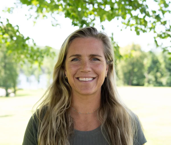 Smiling woman outdoors with green trees in the background.