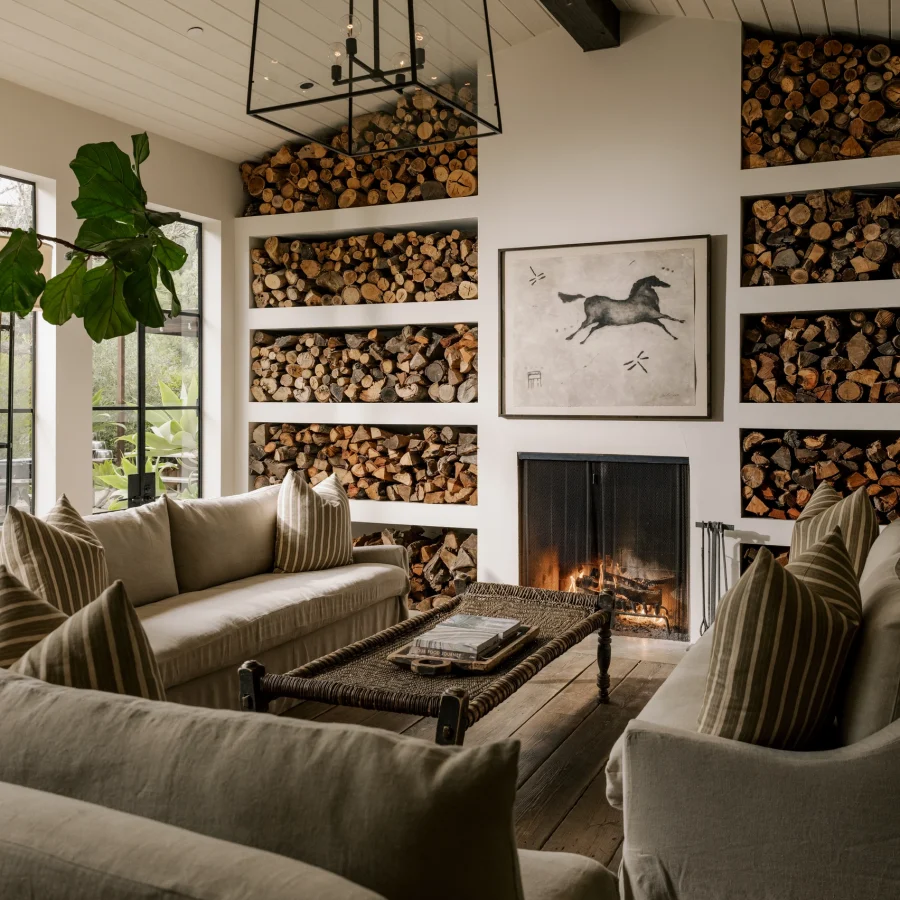 Cozy living room with built-in log storage, beige sofas, and a lit fireplace beneath a black geometric chandelier.