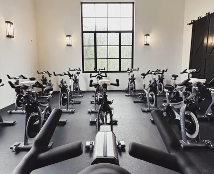 Row of stationary bikes lined up in a bright, minimalist spin studio with a large window at the far wall.