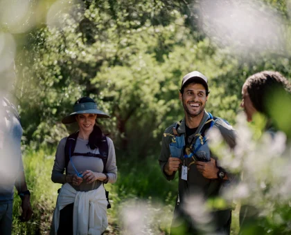 Group of hikers standing on a sunny forest trail, wearing backpacks and outdoor gear, smiling at the camera.