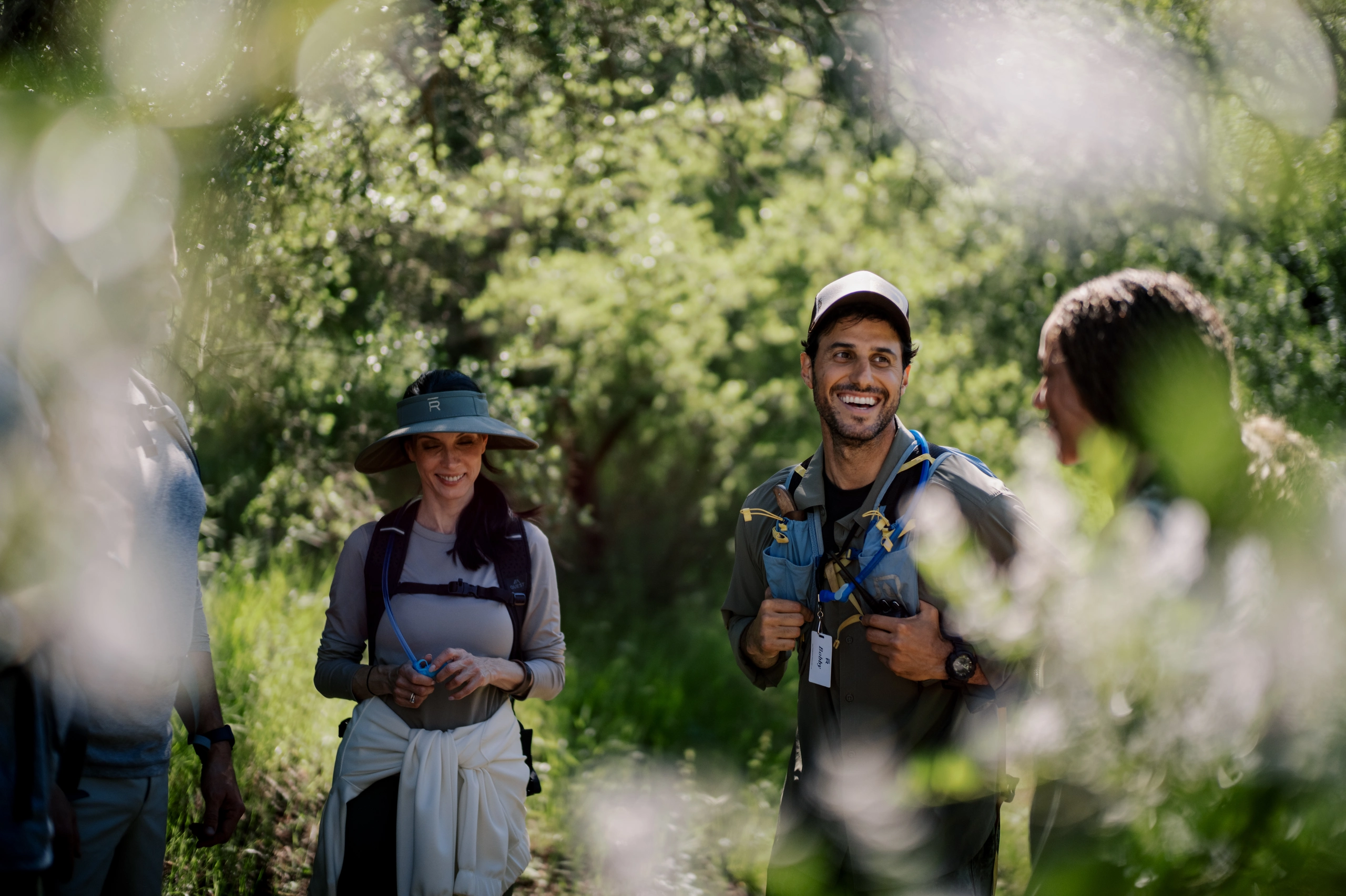 Group of hikers standing on a sunny forest trail, wearing backpacks and outdoor gear, smiling at the camera.