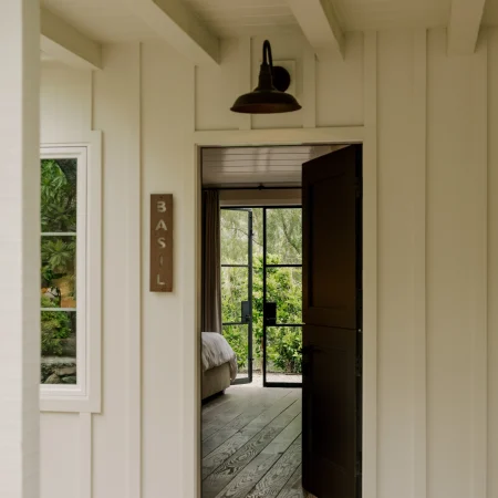 Open doorway to a sunlit interior room; a bronze hanging lamp and a view of a bed through the doorway.