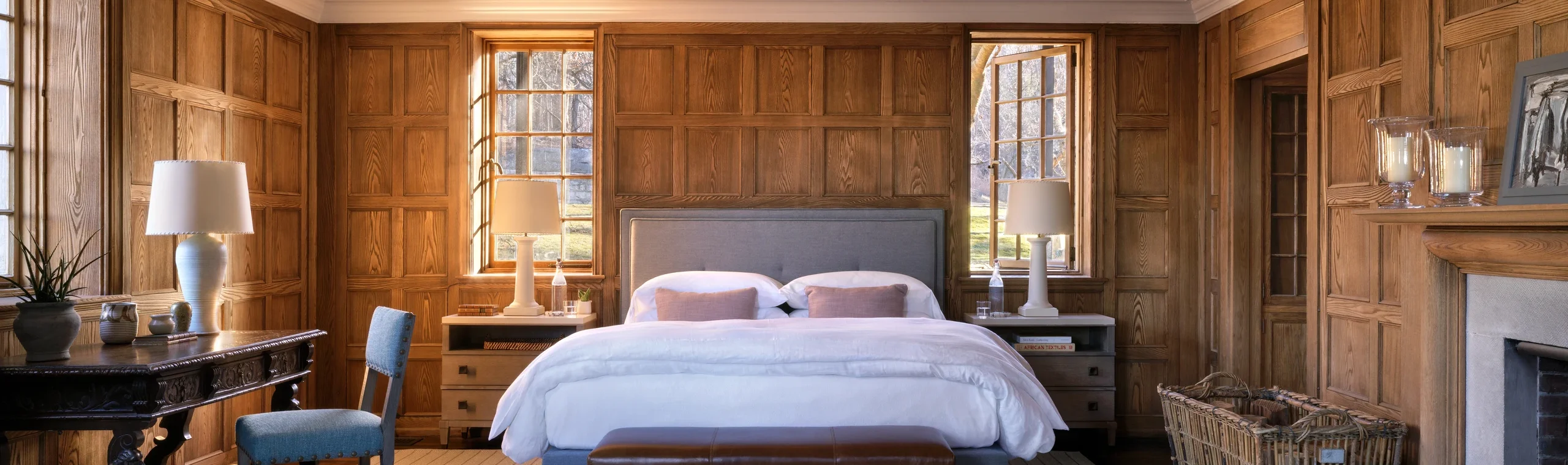 Warm, traditional bedroom with dark wood paneling, two beds, and natural light from windows.