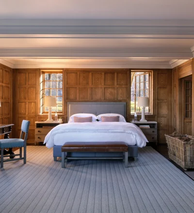 Warm, traditional bedroom with dark wood paneling, two beds, and natural light from windows.