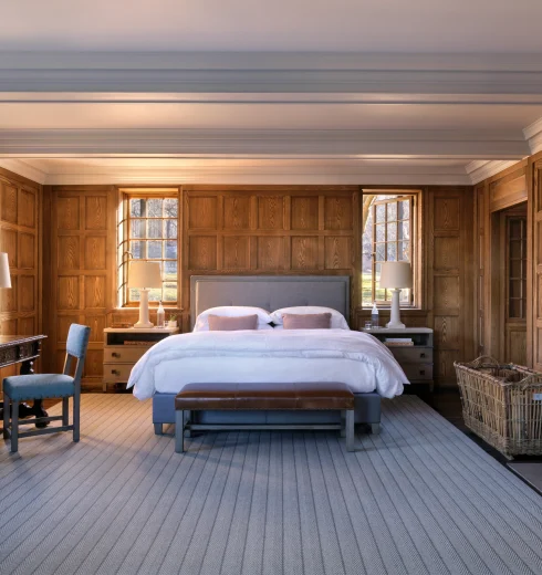 Warm, traditional bedroom with dark wood paneling, two beds, and natural light from windows.