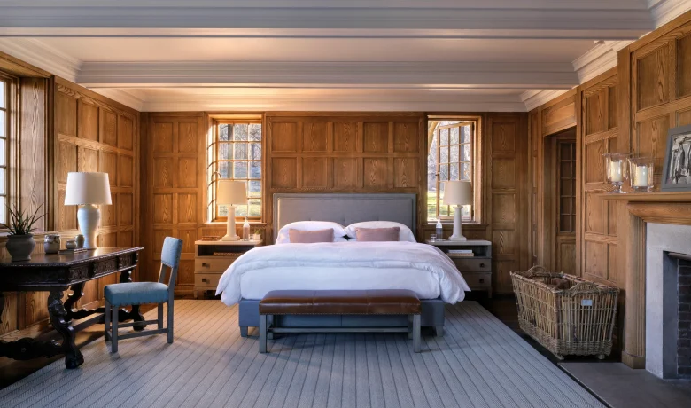 Warm, traditional bedroom with dark wood paneling, two beds, and natural light from windows.