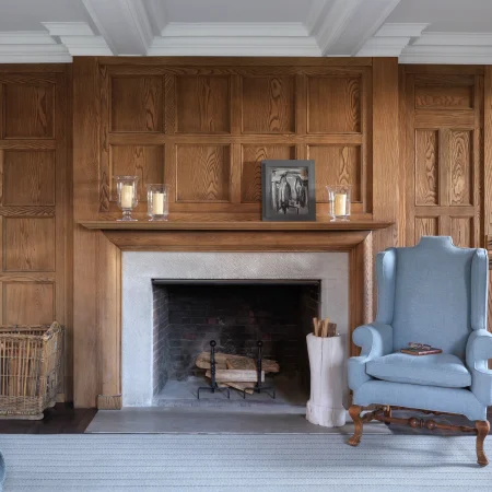 Wood paneled wall above a fireplace with a mantle holding candles and a framed abstract painting; blue upholstered chair to the right.