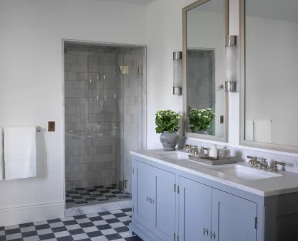 Double-sink bathroom vanity with light blue cabinets, marble countertop, and large mirrors, plus towels and a potted plant on the counter.