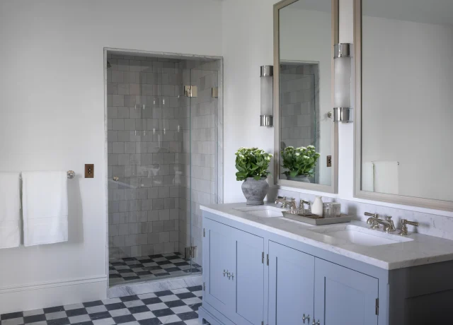 Double-sink bathroom vanity with light blue cabinets, marble countertop, and large mirrors, plus towels and a potted plant on the counter.