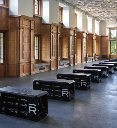 Historic-style gym with wood-paneled walls, tall windows, and rows of black reformer machines along the floor.