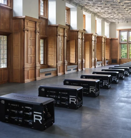 Historic-style gym with wood-paneled walls, tall windows, and rows of black reformer machines along the floor.