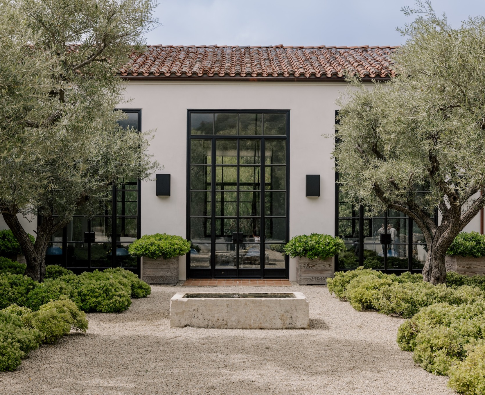 The Ranch Malibu's barn gym, a white stucco building with steel glass doors behind a gravel courtyard and olive trees.