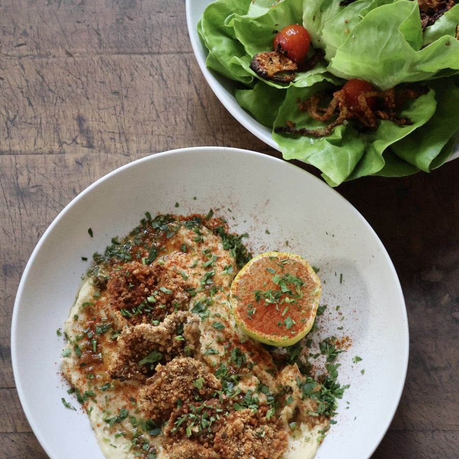 Creamy dish topped with crumbled breadcrumbs, chopped parsley, and sliced hard-boiled eggs on a white plate; a green salad with lettuce is nearby.