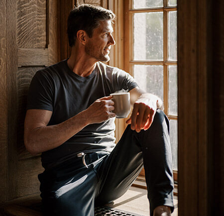 Man drinking coffee in the morning in a wooden window well
