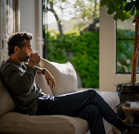 Man drinking coffee on a couch in the morning sunshine