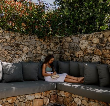 Woman journaling in the corner of a stone bench with cushions